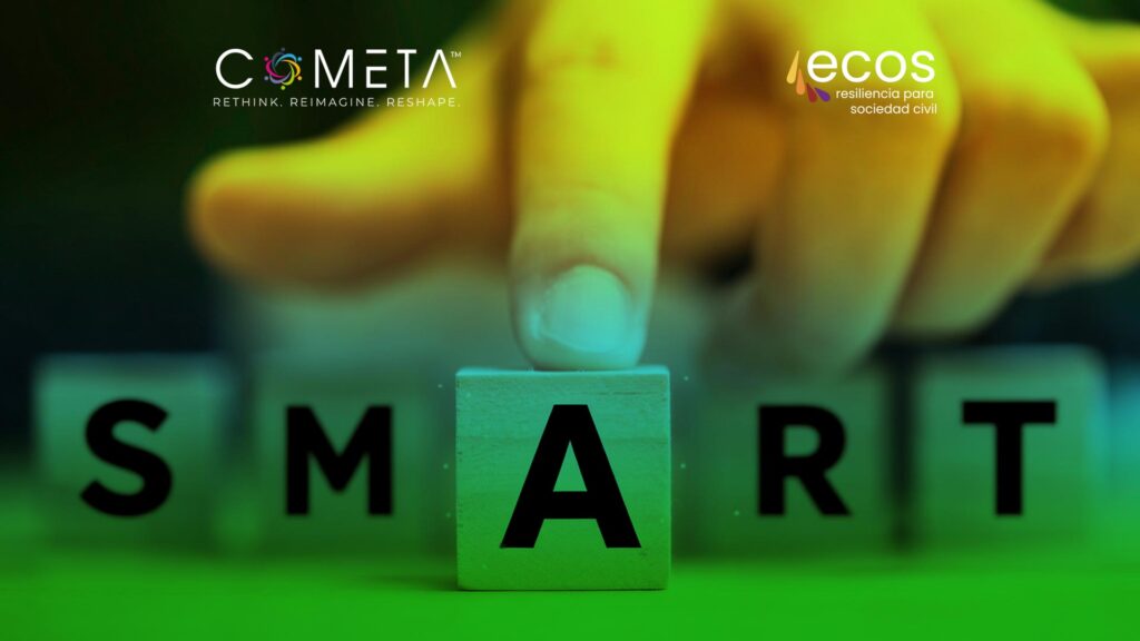 Primer plano de una mano colocando la letra "A" en la palabra SMART, formada con bloques de madera, que representa el concepto de objetivos estratégicos SMART en la planificación organizacional. El logotipo de COMETA aparece en la esquina superior izquierda y el logotipo de ECOS Resiliencia para la Sociedad Civil en la esquina superior derecha.